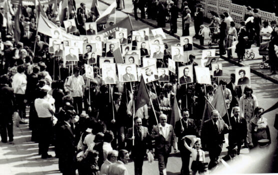 Grupa ludzi podczas pochodu 1-majowego w obrazami ludzi w rękach.