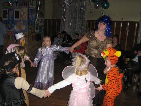Kobieta w niebieskiej peruce tańczy z dziećmi w kółeczku.