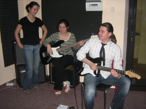 Mężczyzna gra na gitarze z tyłu dwie kobiety. Jedna gra na gitarze.