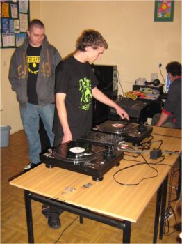 Grupa młodzieży ze sprzętem muzycznym- odtwarzacze , maszyny do miksowania muzyki, komputery. 