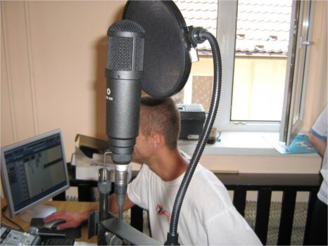 Na pierwszym planie mikrofon w tyle chłopak przy komputerze.
