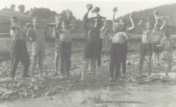 Grupa chłopcó trzyma sporej wielkości kamienie w rękach - szykują się do wrzucenia ich do wody.