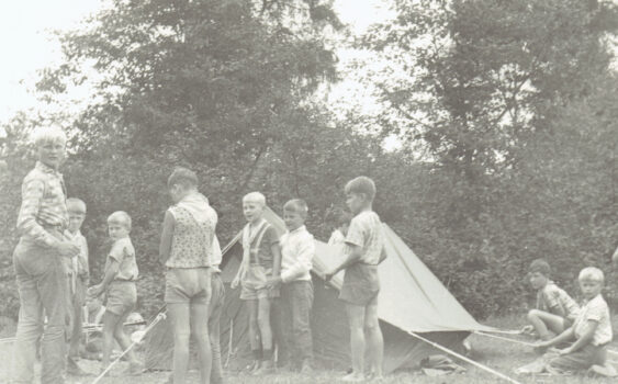 Grupa chłopców rozbija namiot na leśnej polanie.