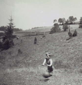 Chłopiec na łące łapie piłkę.