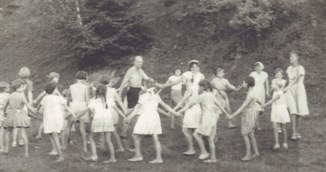 Mężczyzna i gruoa dzieci trzymają się za ręce i tańczą w kółeczku.