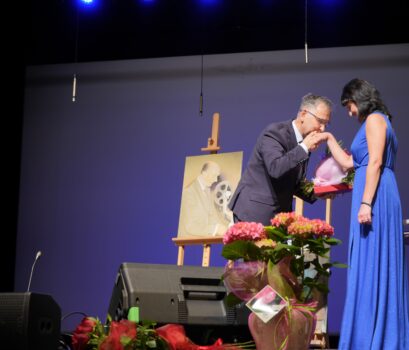 Mężczyzna całuje kobietę w rękę i daje jej kwiaty i podziękowania- na scenie.