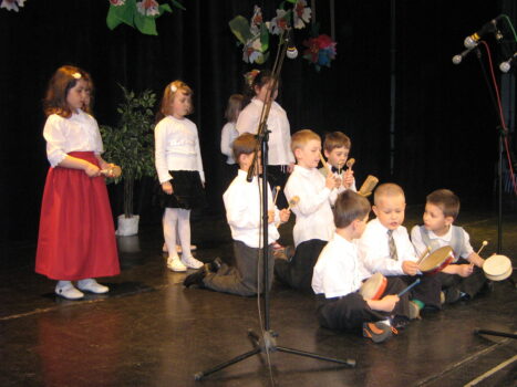 Dzieci w odświętnych strojach spiewaja na scenie