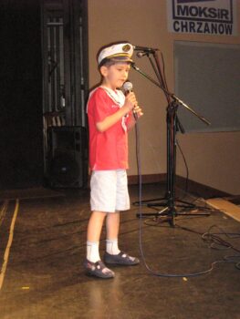 Chłopiec na scenie w marynarskim ubraniu. Chłopiec coś śpiewa.