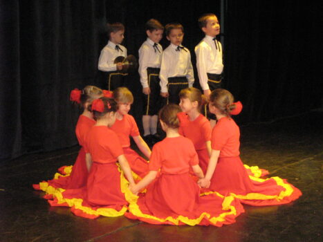 Grupa dziewczynek w czerwonych sukniach i chłopcy w białych bluzkach nas scenie