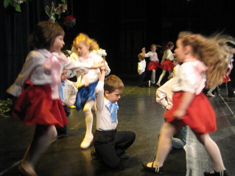 Grupa dzieci tańczy na scenie. Rozwiane włosy i spódnice.