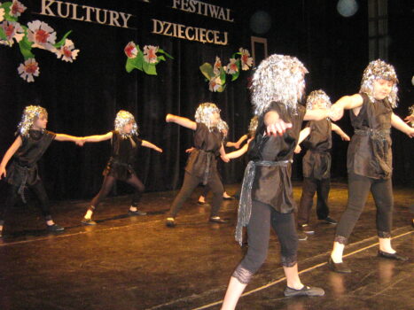 Dziewczęta w błyszczących perukach tańczą na scenie.