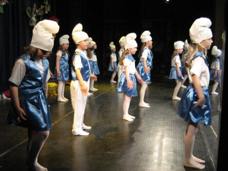 Dzieci w przebraniu smerfów tańczą na scenie.