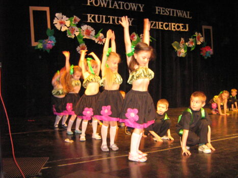 Dzieci w kolorowych strojach tańczą na scenie.