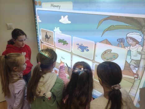 Dzieci przy tablicy interaktywnej ćwiczą słówka grając w interaktywne memory.