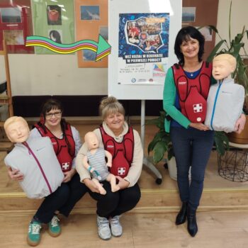 Pracownicy PMDK zachęcają do akcji bicia rekordu w pierwszej pomocy. Ubrani w kamizelki treningowe do nauki reagowania w sytuacji zadławień i zakrztuszeń, w rękach trzymają fantomy ćwiczebne.