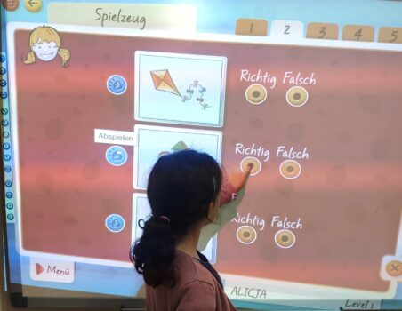 Dziewczynka przy tablicy interaktywnej ćwiczy rozumienie ze słuchu rozwiązując zadanie prawda/fałsz.