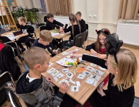 Dzieci podczas zajęć języka angielskiego pracują w grupach przyporządkowując podpisy do obrazków. Niektóre osoby są przebrane w stroje Halloween.