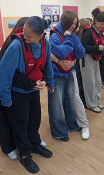 Młodzi ludzie ćwiczą rękoczyn Heimlicha w specjalnych kamizelkach treningowych.