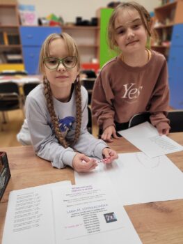 Dwie dziewczynki podczas zajęć języka polskiego, czytają tekst i piszą.