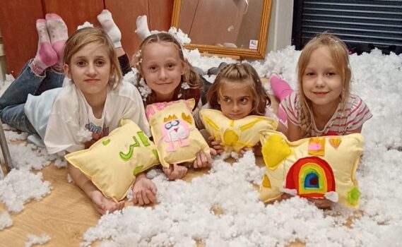 Dzieci z uszytymi przez siebie poduszkami leżą w białym puchu.