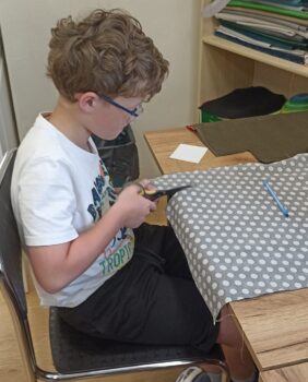 Chłopiec wycina materiał w kropki podczas zajęć szycia na maszynie.