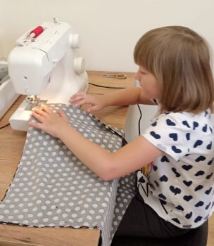 Dziewczynka szyje na maszynie, materiał w kropki.
