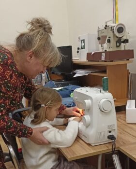 Dziecko przy maszynie do szycia wraz z nauczycielem.