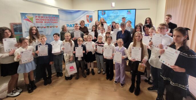 Grupa uczestników eliminacji powiatowych konkursu recytatorskiego. Młodzi stoją z dyplomami w sali odczytowej PMDK.